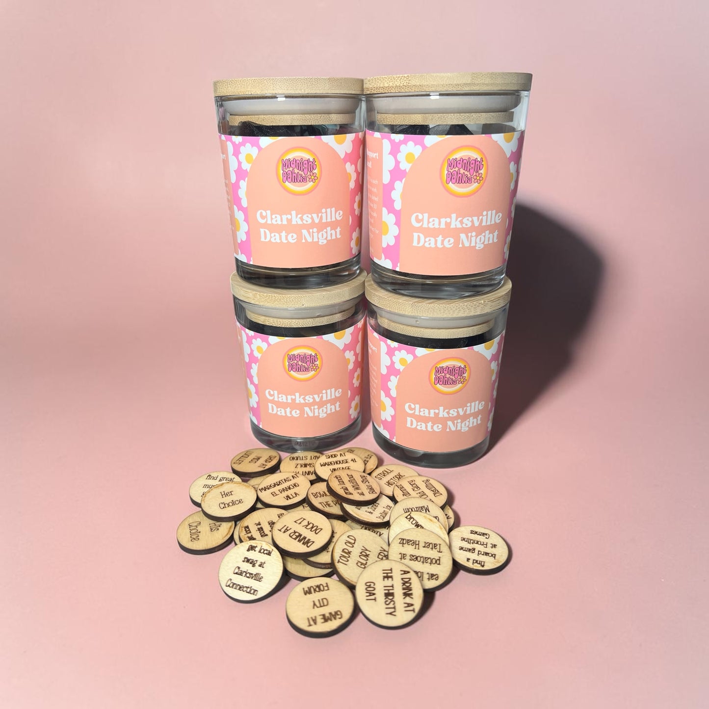 Four candles labeled 'Clarksville Date Night' with wooden tokens on a pink background
