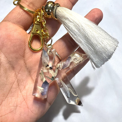 a letter k resin keychain with blue flowers and a white tassel, held by a hand