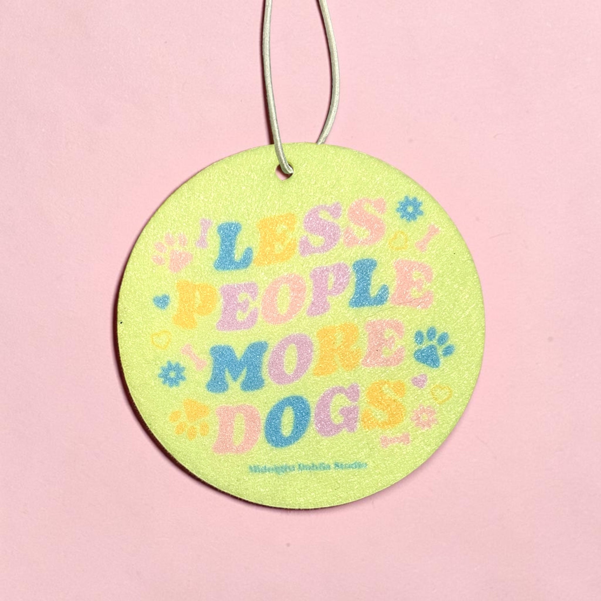 Round green tag with colorful text 'LESS PEOPLE MORE DOGS' on a pink background