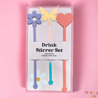 three drink stirrers with the top shaped in a daisy, butterfly, and heart in lavender purple, iridescent, and pink coral.