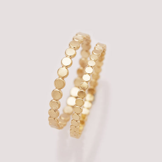 Two gold ring bands with a beaded design on a light gray background
