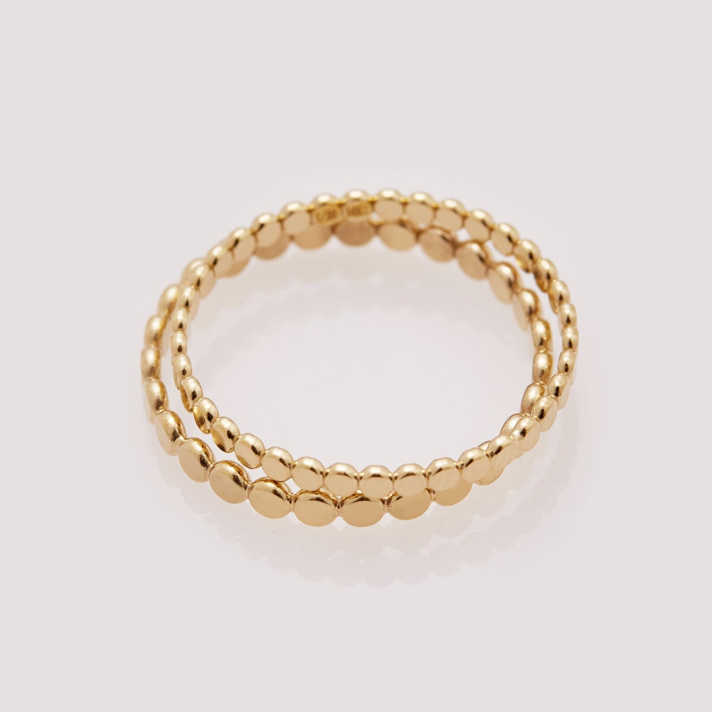 Two gold beaded rings stacked on a light gray background