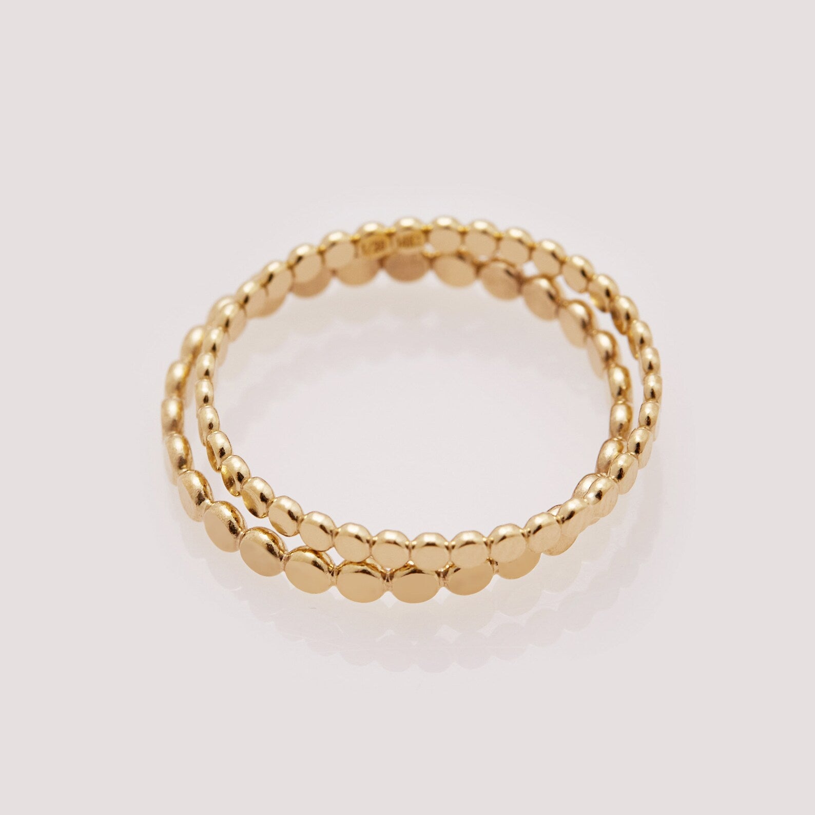 Two gold beaded rings stacked on a light gray background