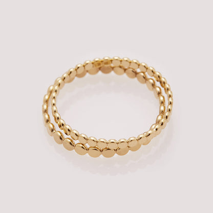 Two gold beaded rings stacked on a light gray background