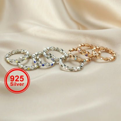 gold and silver rings with embedded stones on a beige fabric background, featuring a '925 Silver' label.