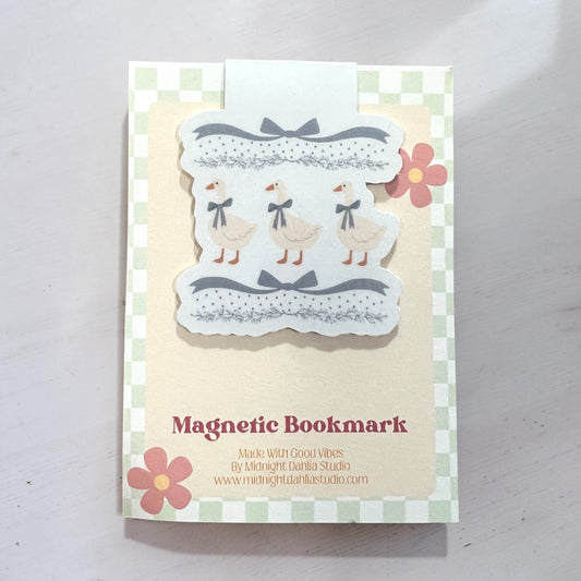 A handmade magnetic bookmark card featuring three cute cream-colored ducks wearing blue bows, set against a green and white checkered border with pink flowers. The card is labeled 'Magnetic Bookmark' and shows the brand 'Midnight Dahlia Studio'.