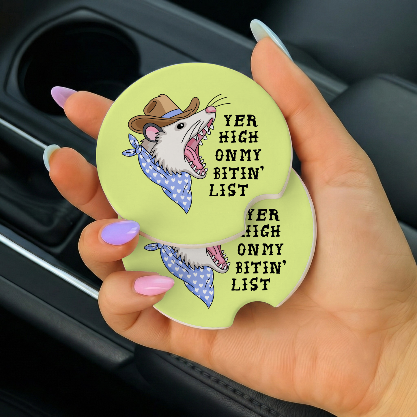 Hand holding a car coaster with a cartoon rat design and text.
