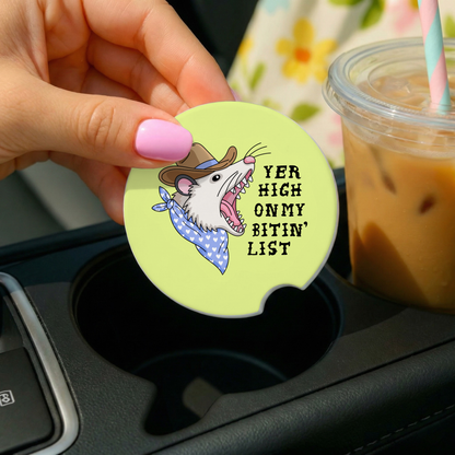 Coaster with cartoon rat design and text in a car cup holder with iced coffee.