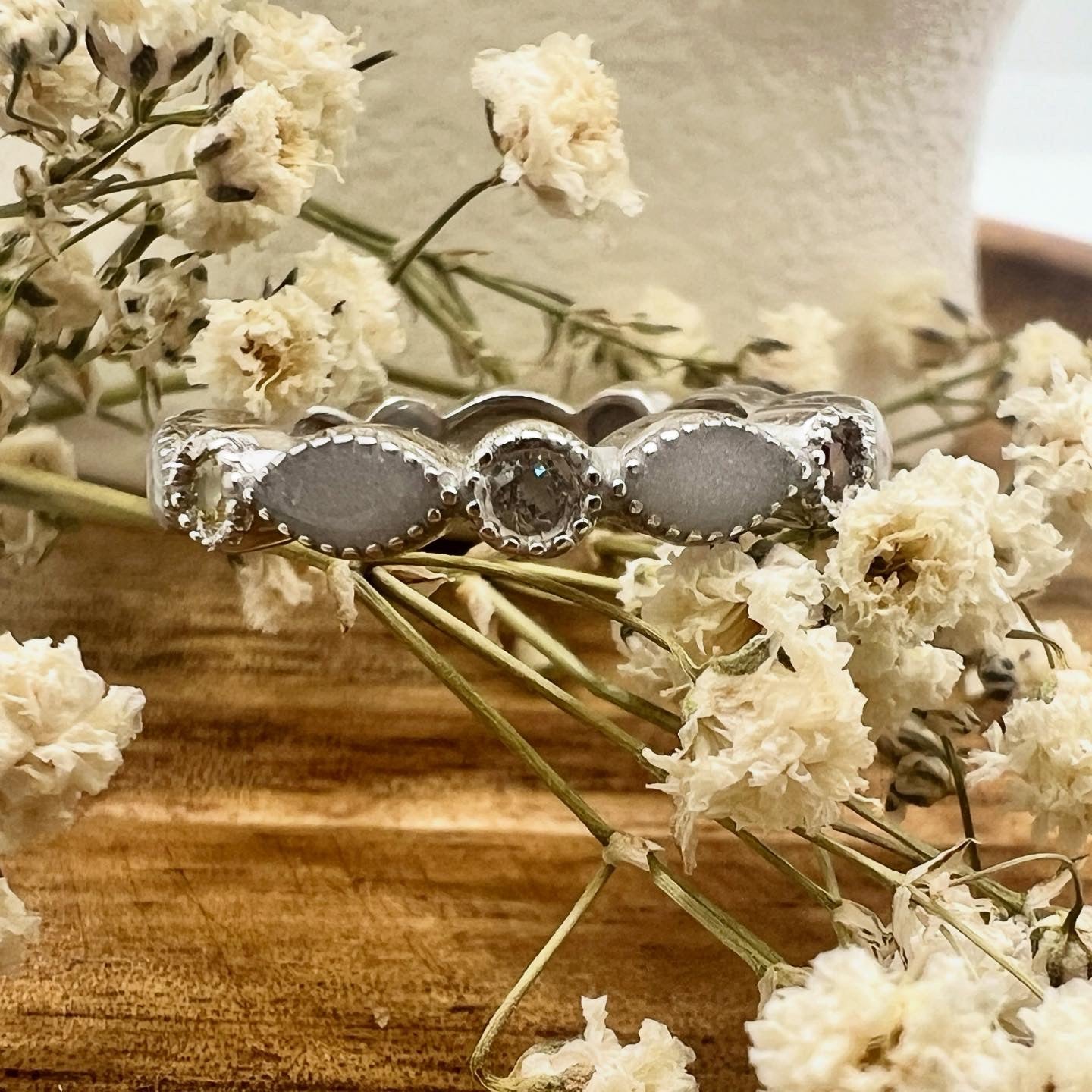 Silver ring with three stones on a wooden surface with white flowers