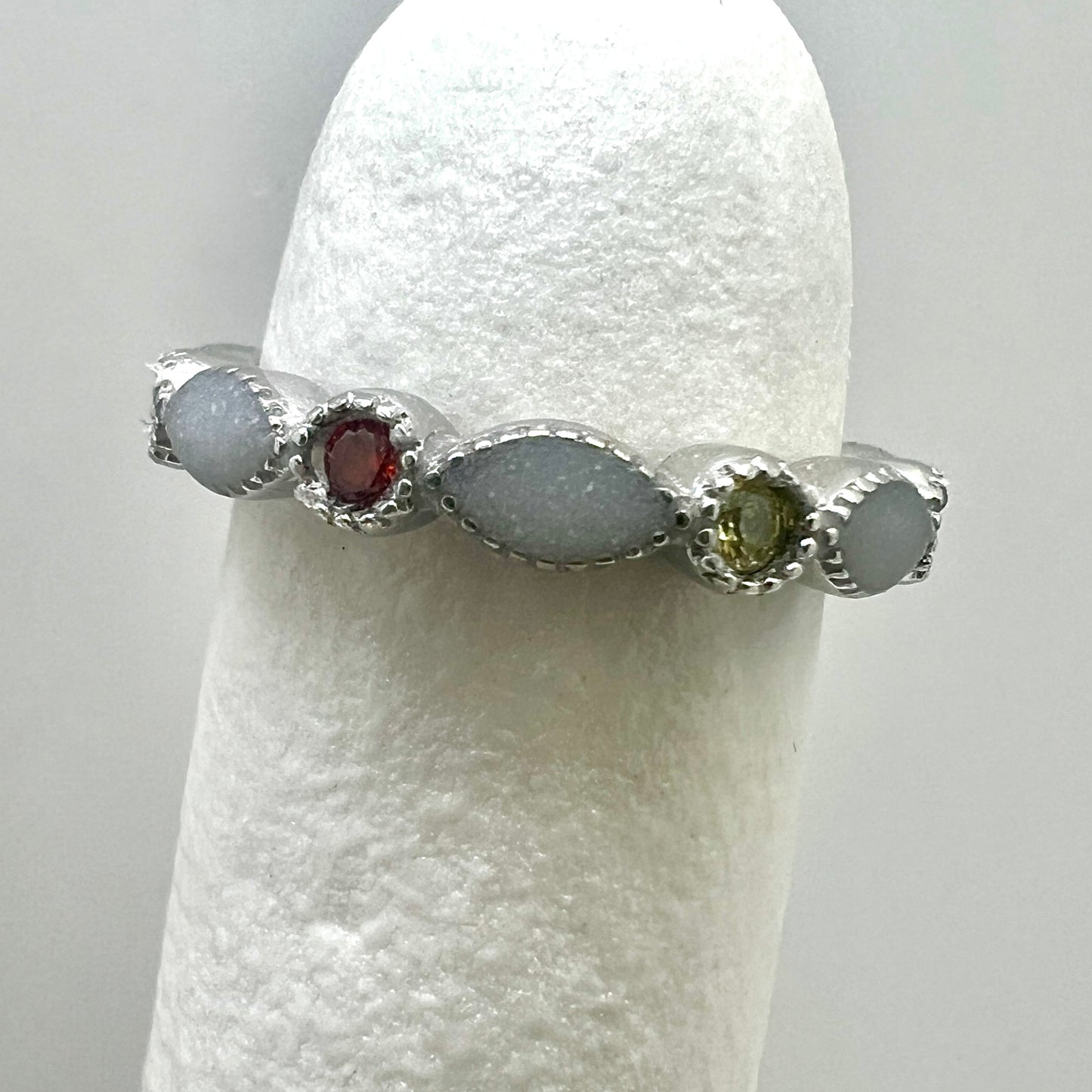 Silver ring with embedded stones on a white stand