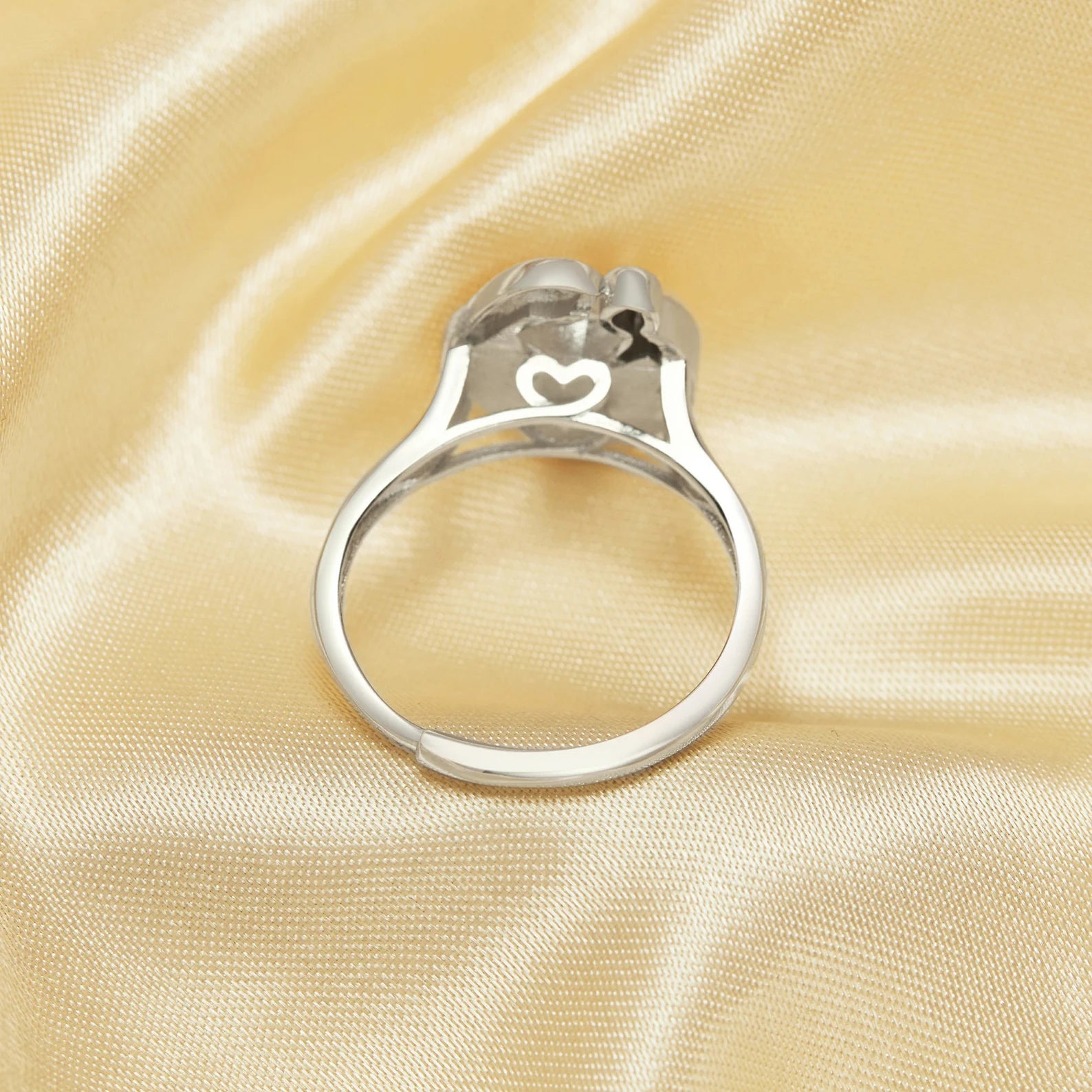 Silver ring with a heart-shaped design on a beige satin background