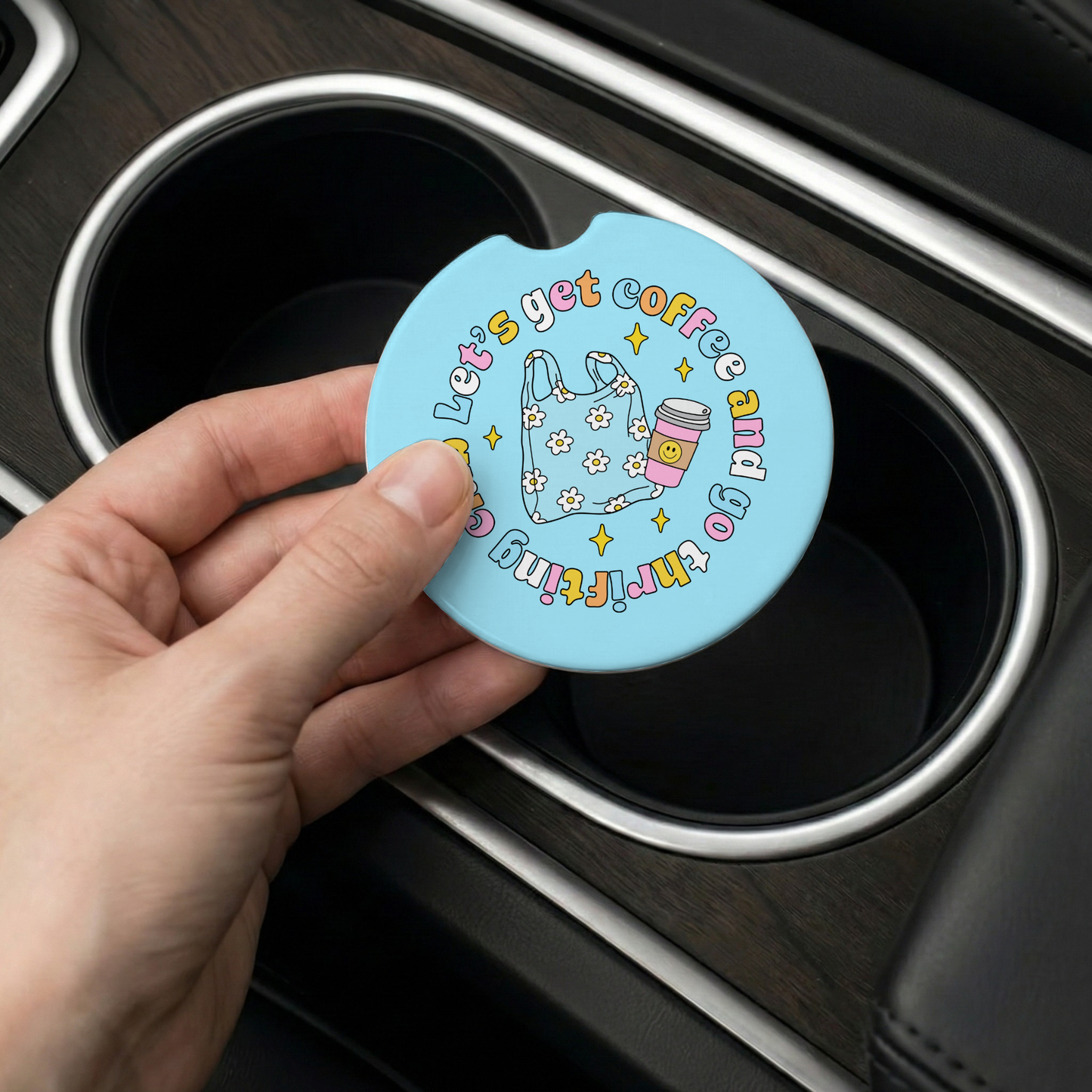 Hand holding a blue car coaster with text and graphics over a car's cup holder.