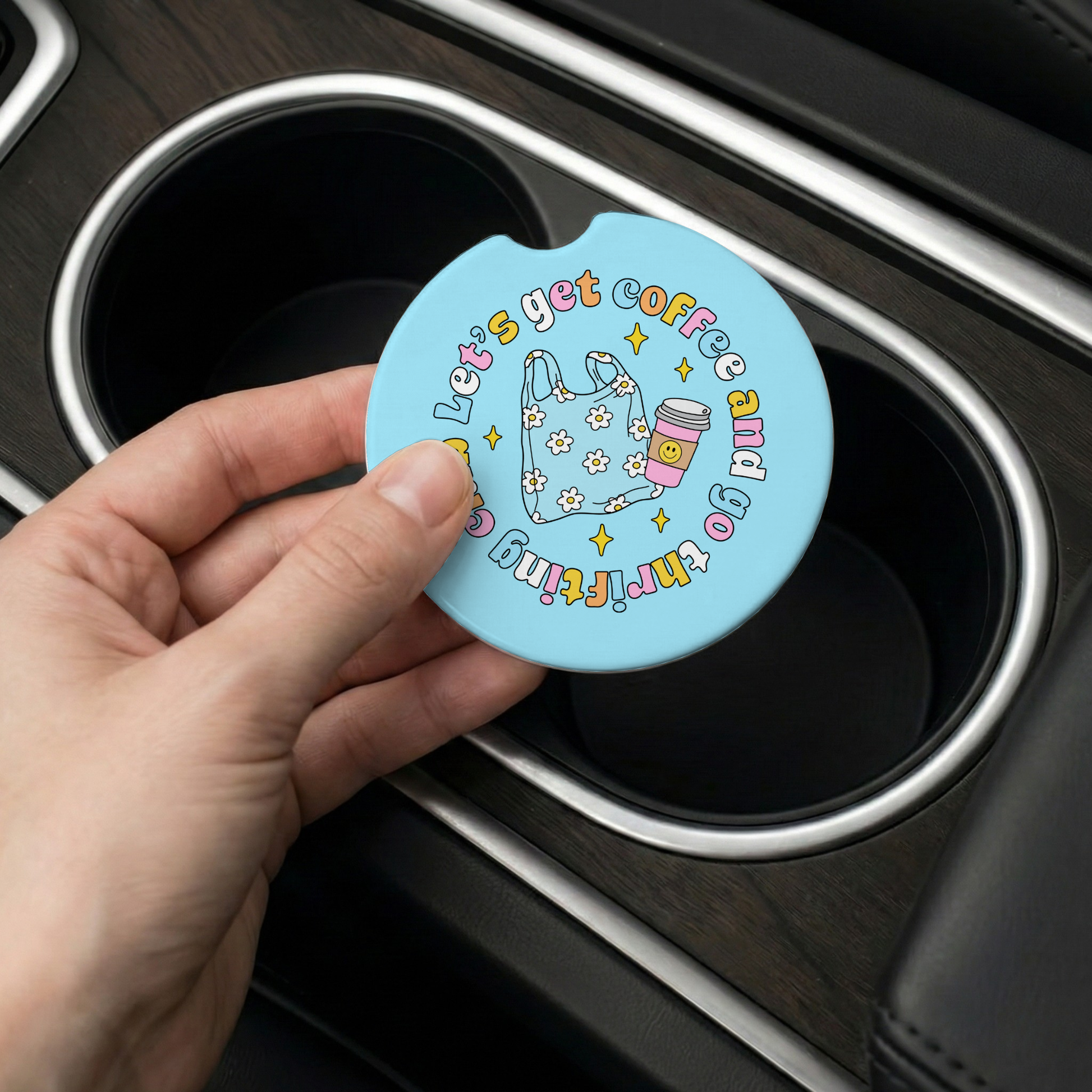 Hand holding a blue car coaster with text and graphics over a car's cup holder.