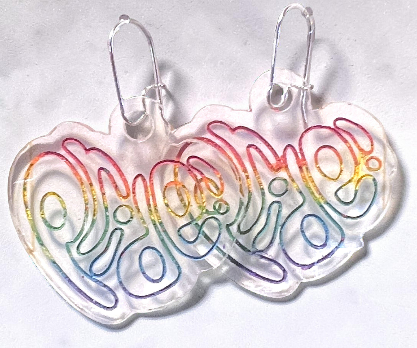 Heart-shaped earrings with 'Pride' in rainbow colors on a light gray background