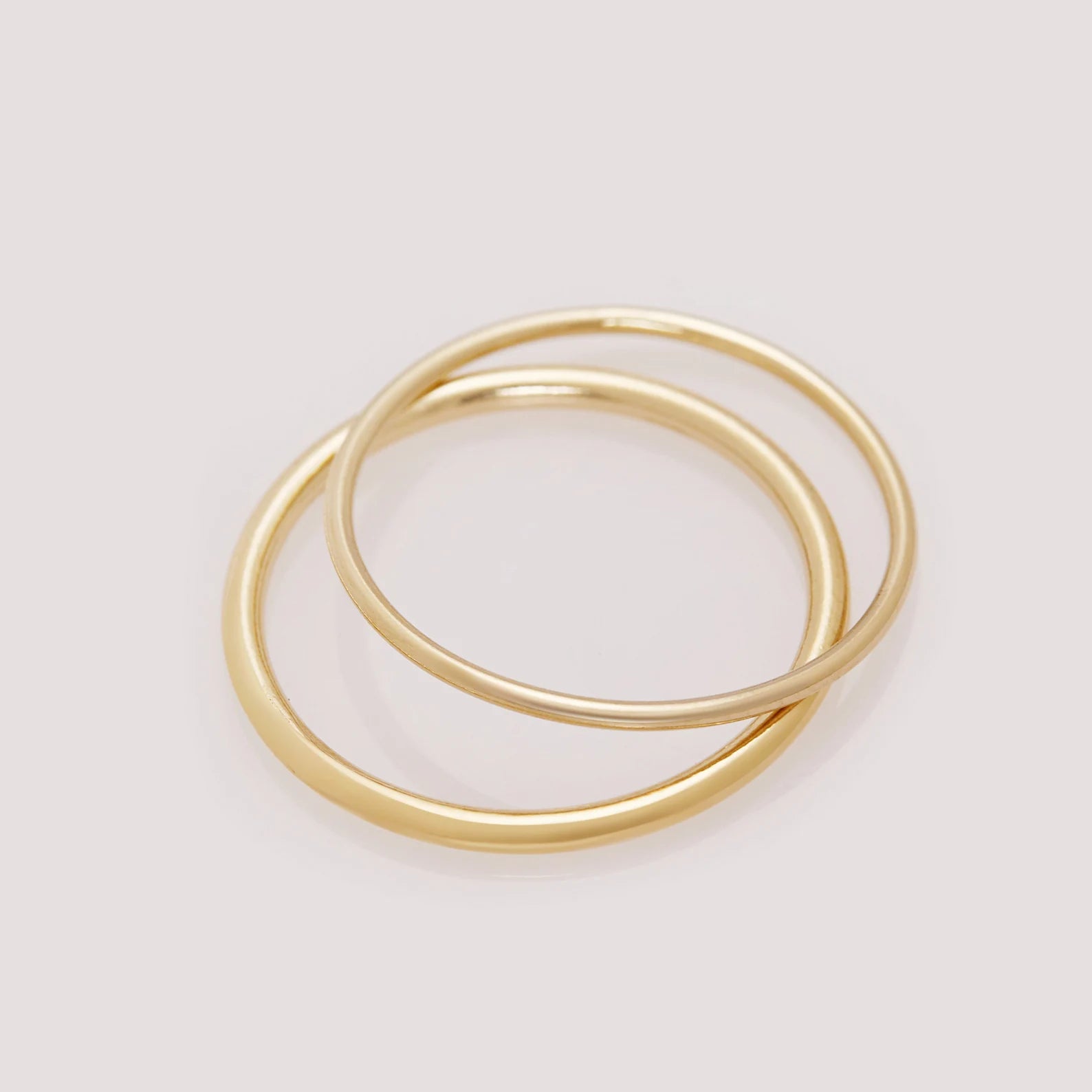 Two gold rings stacked on a light gray background
