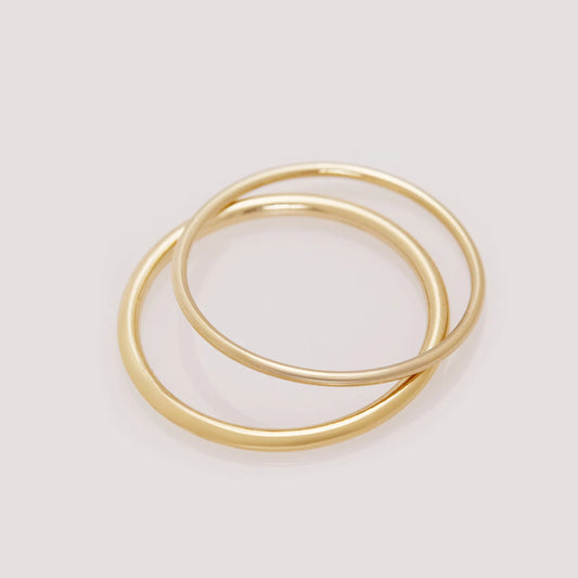 Two gold rings stacked on a light gray background