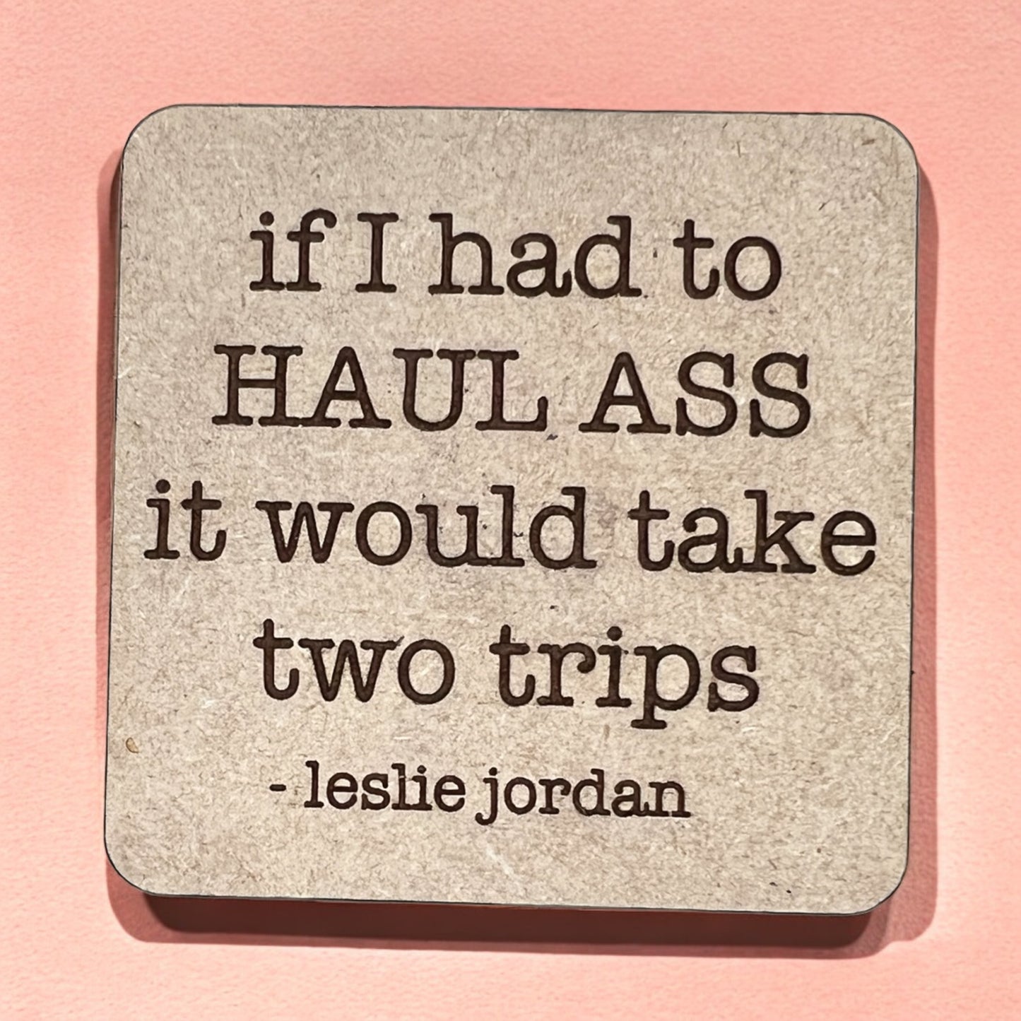 A square magnet with a humorous quote printed on it, placed against a pink background.