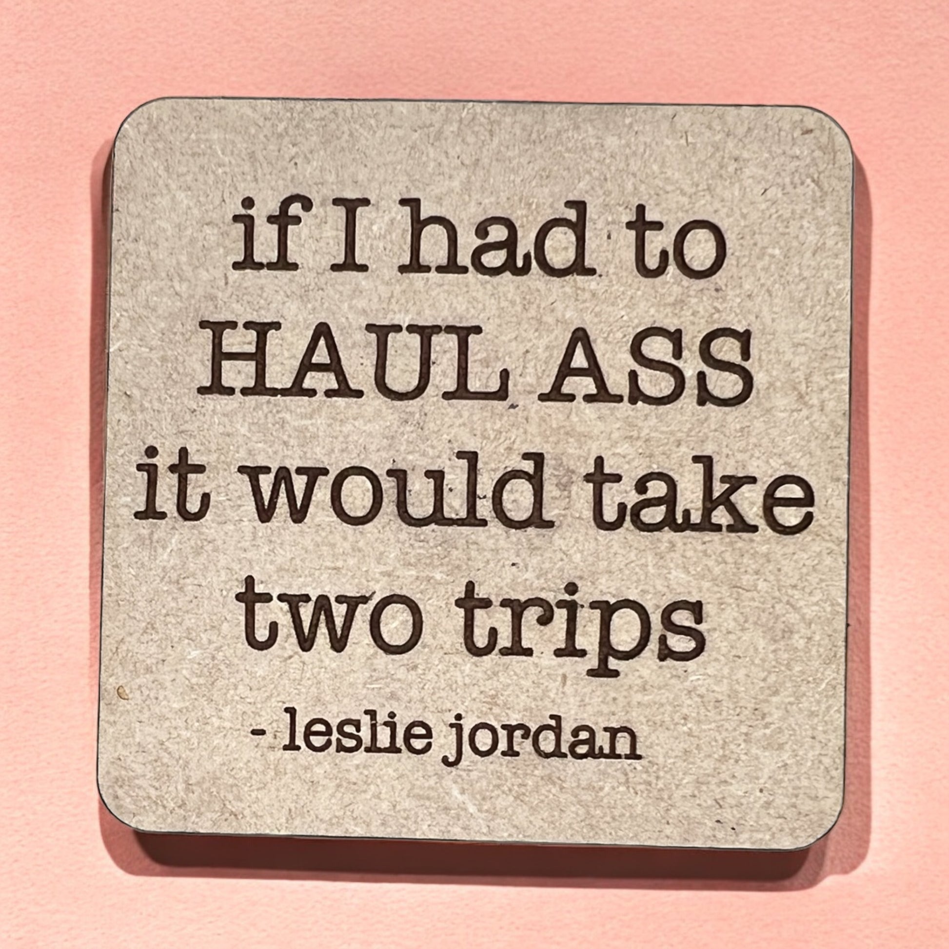 A square magnet with a humorous quote printed on it, placed against a pink background.