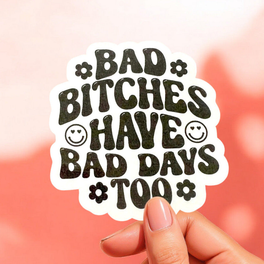a white sticker with black text that reads bad bitches have bad days too with smiley faces and daisies