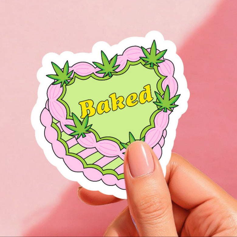 A colorful sticker with a pink and green cake design and the word 'Baked' written in the center, decorated with cannabis leaf motifs.