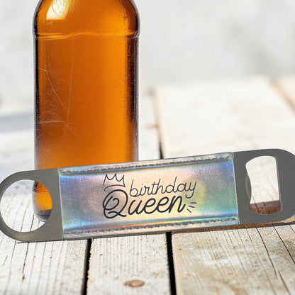 Bottle opener with 'Birthday Queen' text next to a bottle on a wooden surface