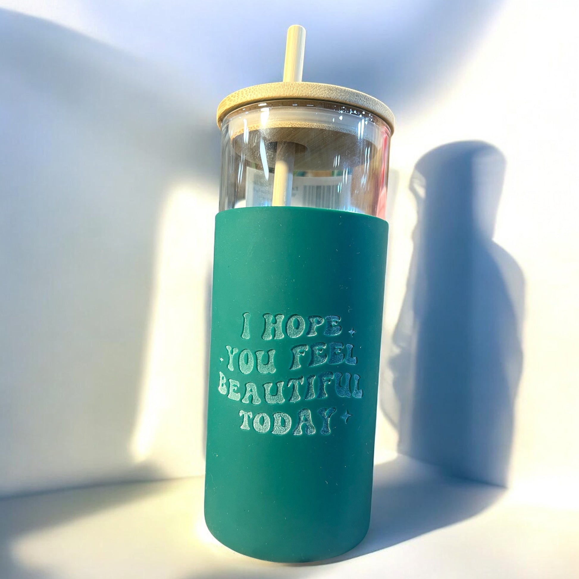 A green tumbler with a clear glass body, a silicone engraved floral design, a bamboo straw, and the text 'i hope you feel beautiful today'
