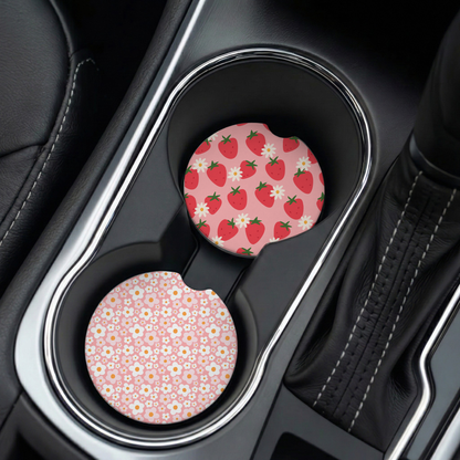 Two pink car cup holders with strawberry and daisy pattern in a car's cup holder.