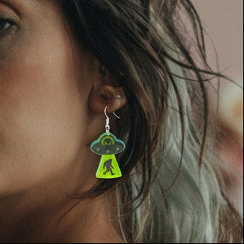 Woman with tattoos and green earrings against a blurred floral background