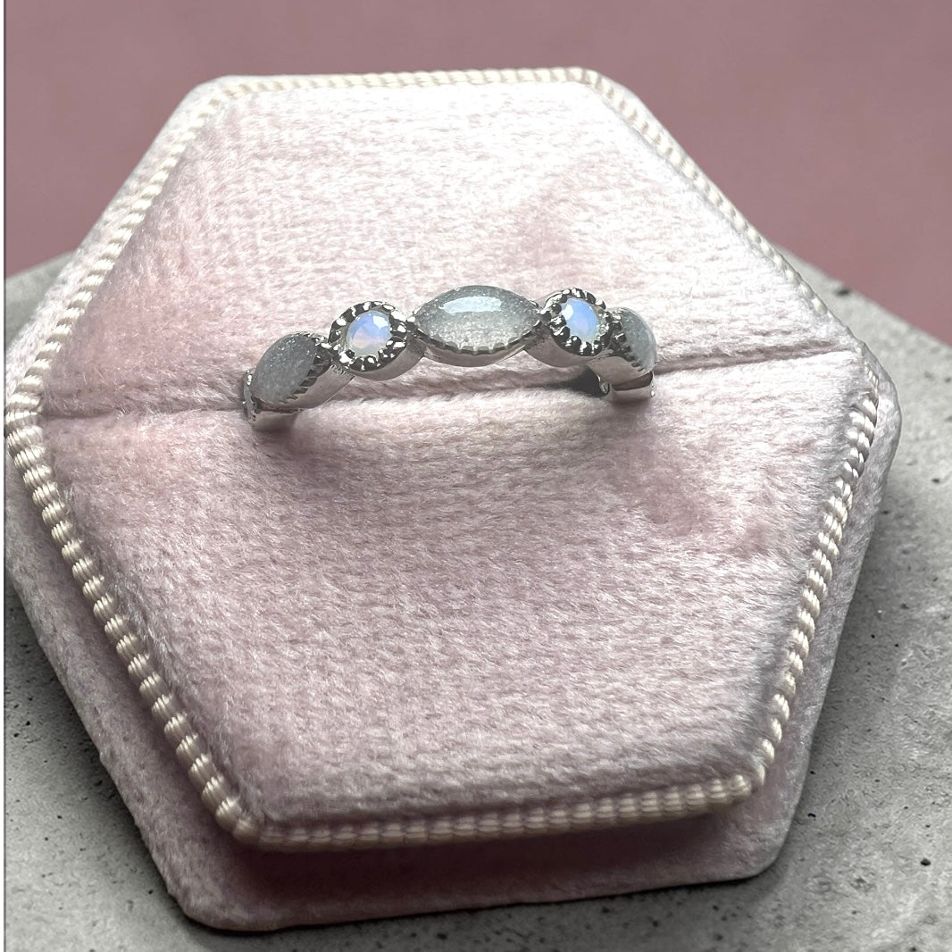 Silver ring with three gemstones on a pink velvet cushion