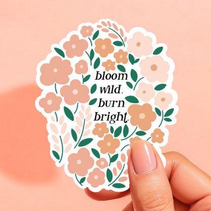 A sticker with peach and orange blooms that reads bloom wild, burn bright.
