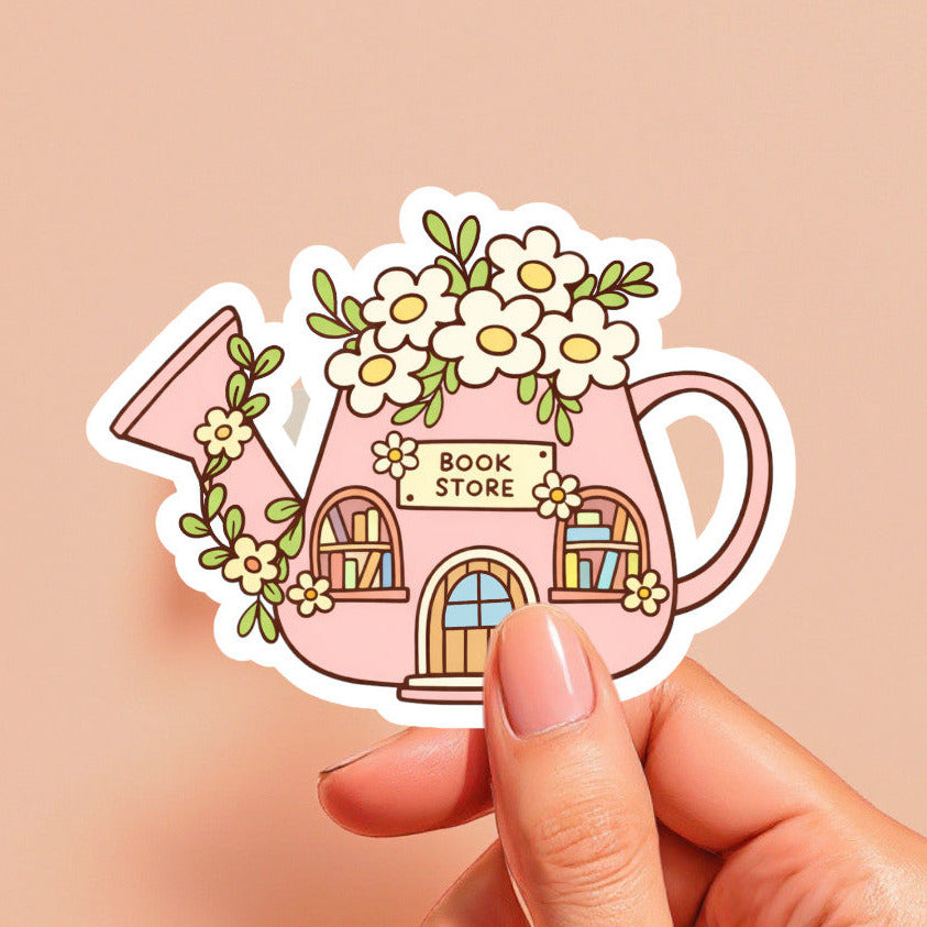 Sticker of a pink watering can with a book store design held by a hand against a beige background