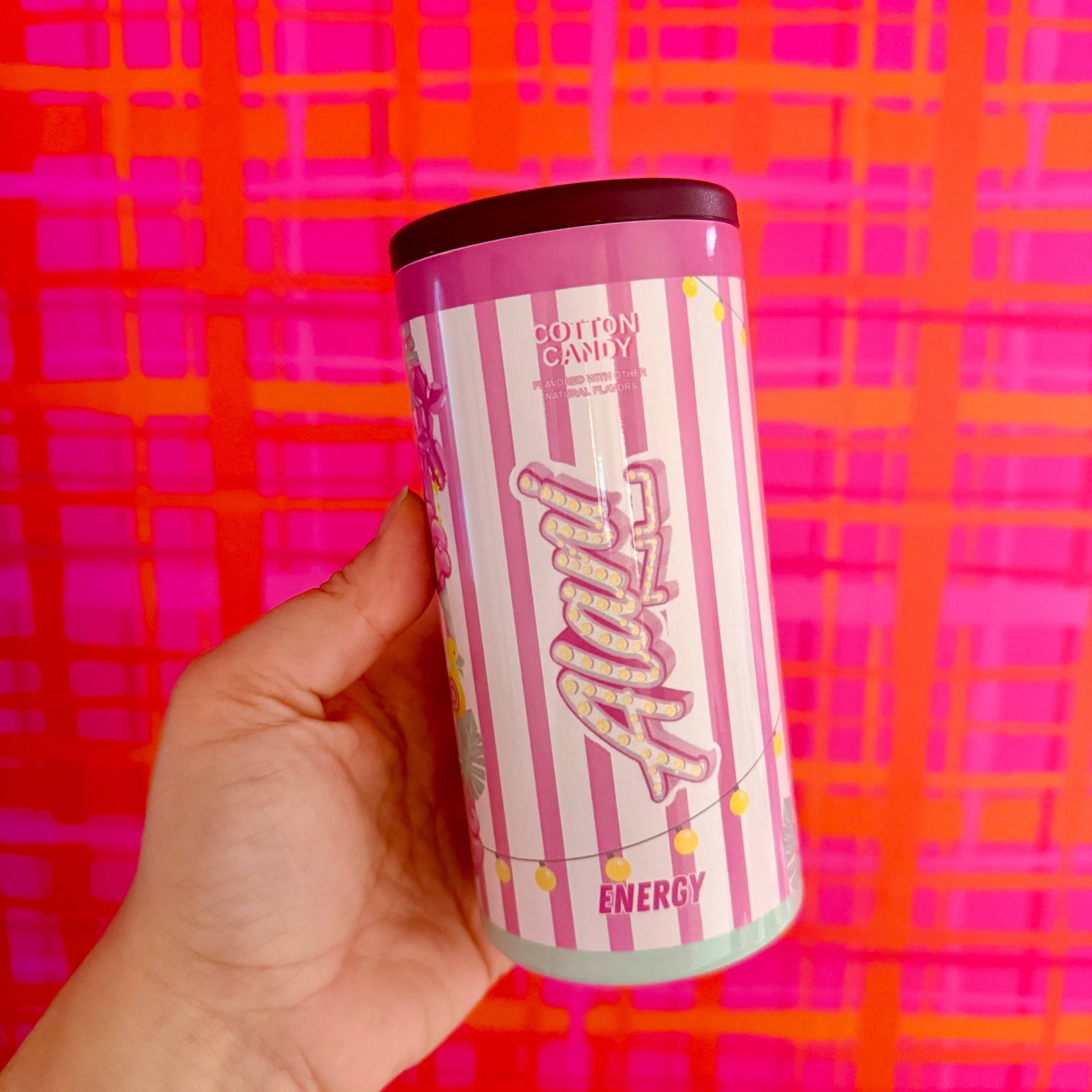 Hand holding a pink and white striped energy drink can against a colorful background