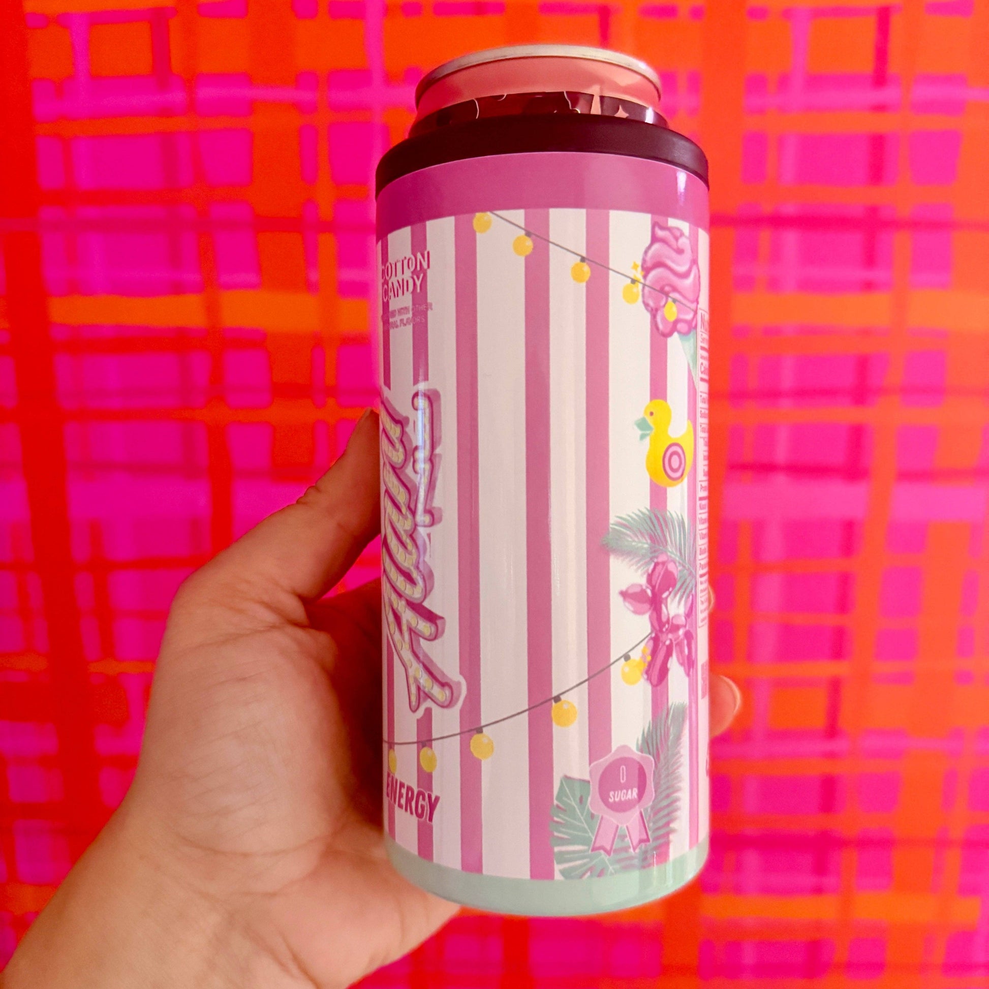 Hand holding a pink energy drink can against a colorful geometric background
