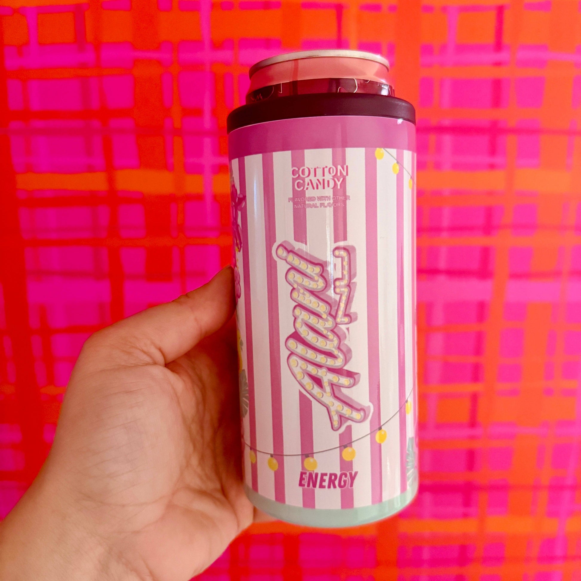 Hand holding a pink and white energy drink can against a colorful background