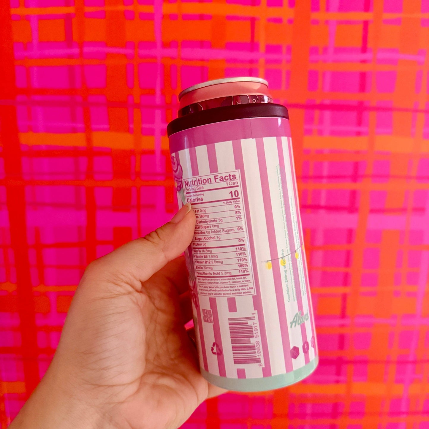 Hand holding a pink and white can against a pink and orange checkered background