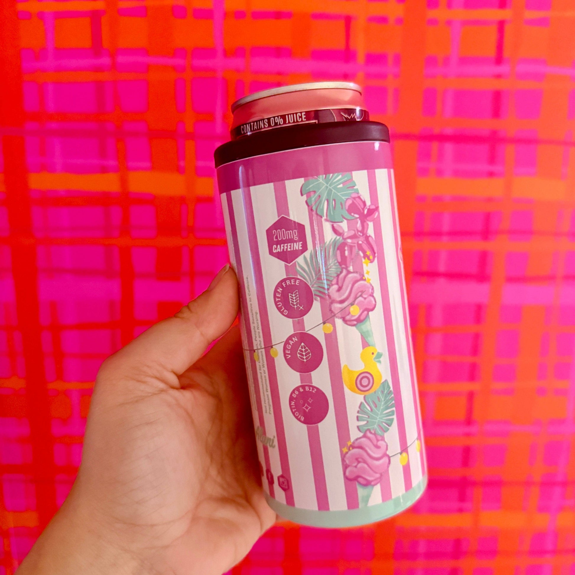Hand holding a colorful can against a pink and orange checkered background