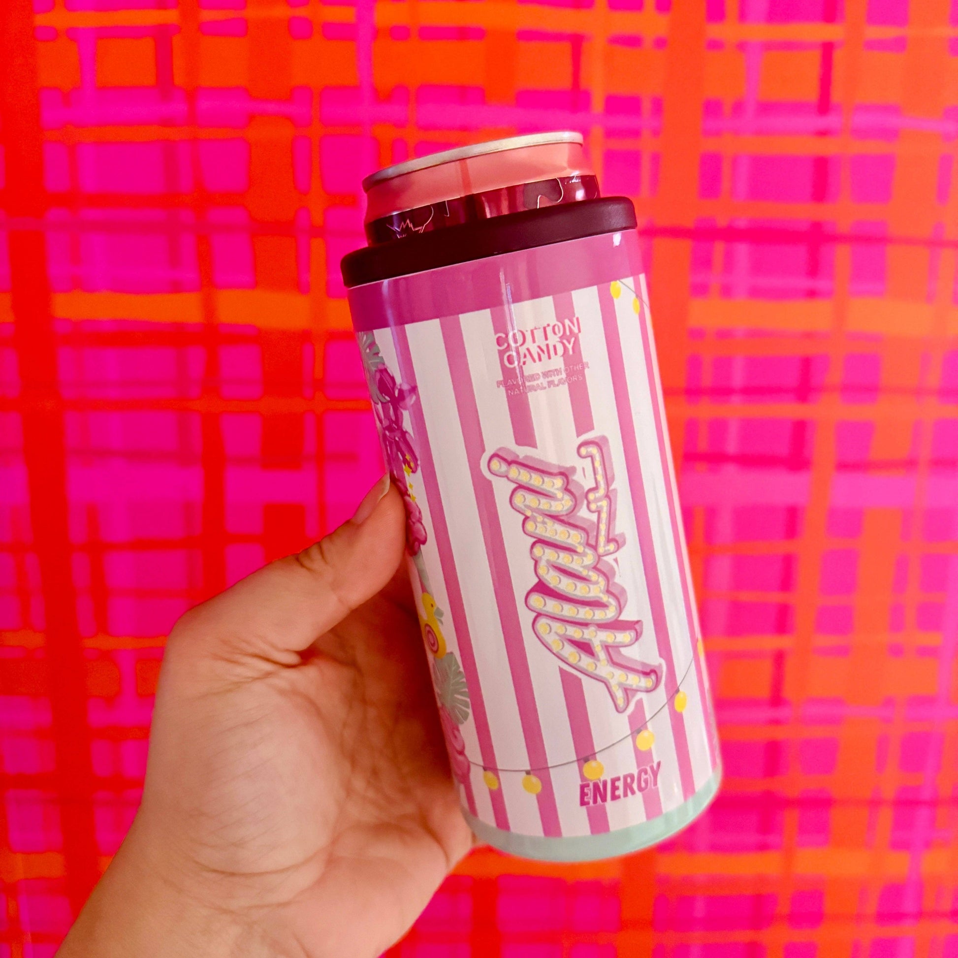 Hand holding a pink and white energy drink can against a colorful patterned background
