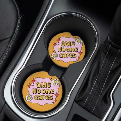 Two car cup holders with 'OMG No one cares' coasters in a vehicle interior.
