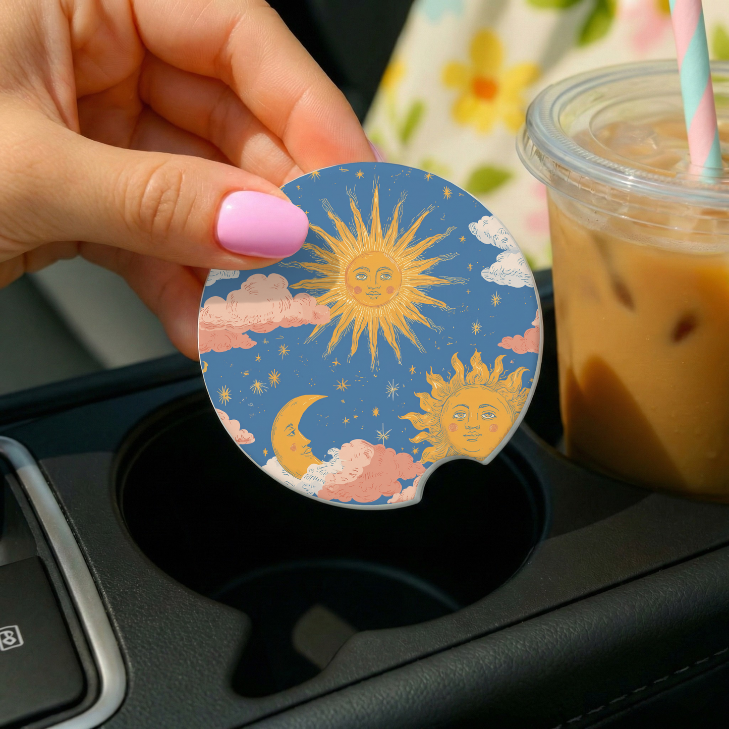 Hand holding a car coaster with sun and moon design over a cup holder, with a drink in the background.