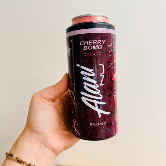 Hand holding a can of 'Cherry Bomb' energy drink with 'Alani' branding on a plain background