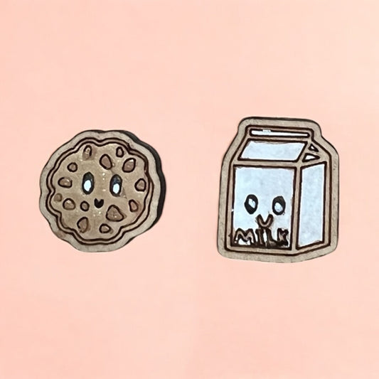 Two cartoon-style earrings, one of a cookie and one of a milk carton, on a pink background.