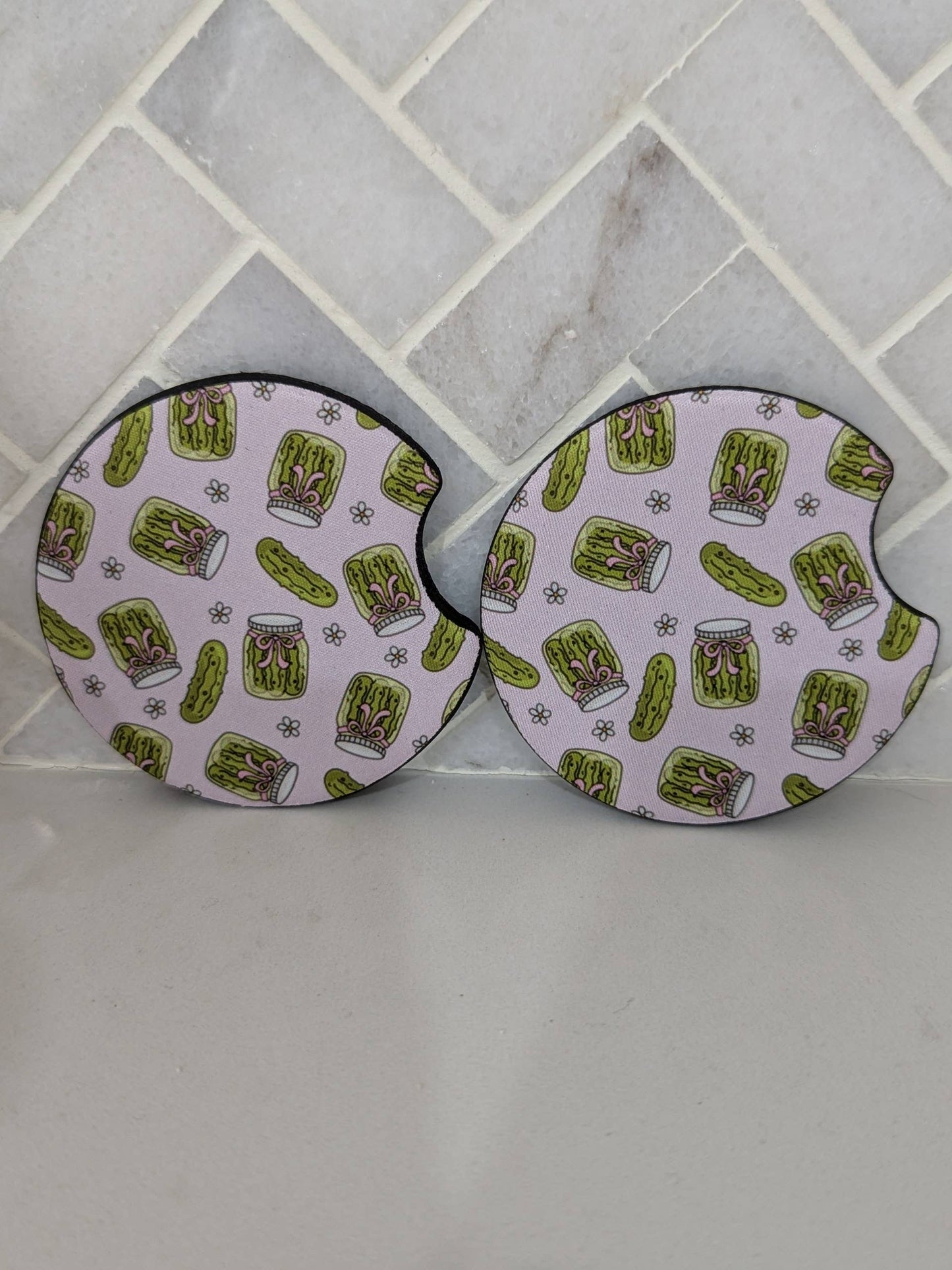 Two round coasters with pickle pattern on a tiled surface