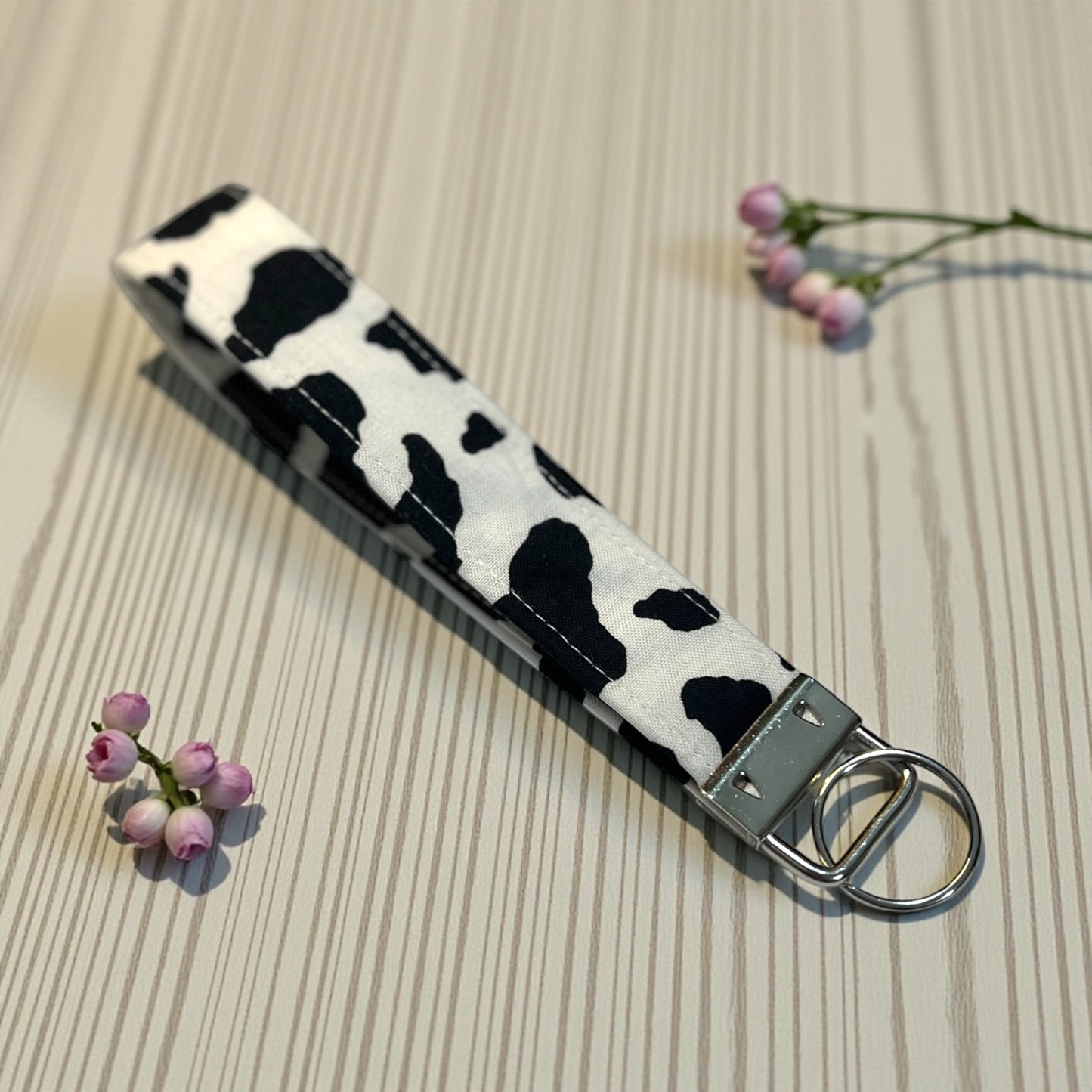 Keychain with cow print pattern on a textured surface with flowers.