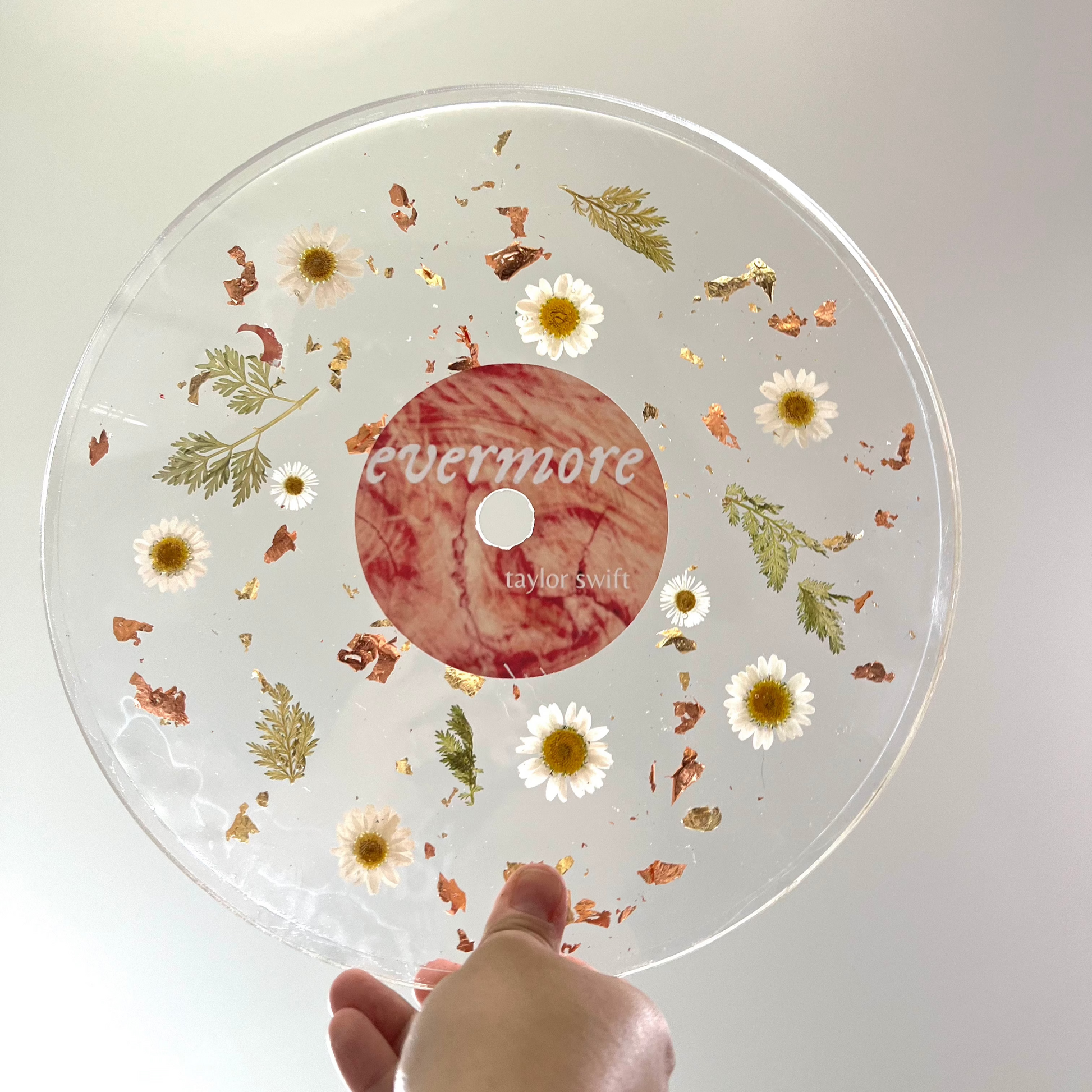 A custom decorative resin record made with white daisies , green leaves , and gold flake.  It has a label to make it look like a Taylor Swift album.