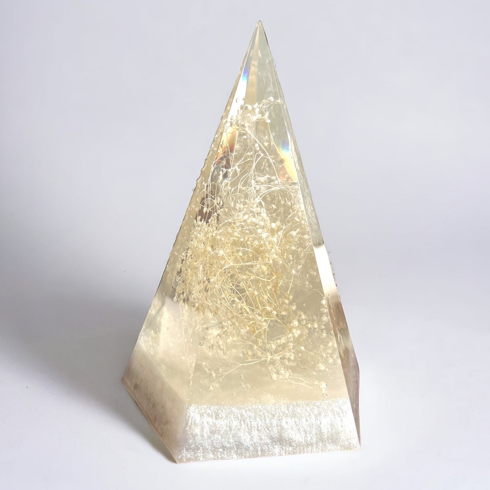 a clear resin pyramid shaped ring holder with dried white babys breath inside against a white background