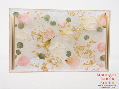 a clear resin serving tray filled with pink and white flowers, gold flake, and has gold handles against a white background