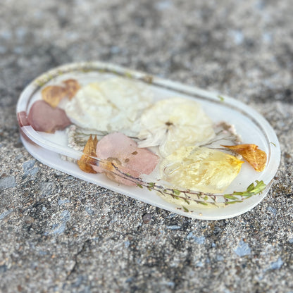 A custom vanity tray filled with dried pressed flowers including white roses , pink rose petals , and yellow and gold flowers.  It is made of crystal clear resin with a white base.