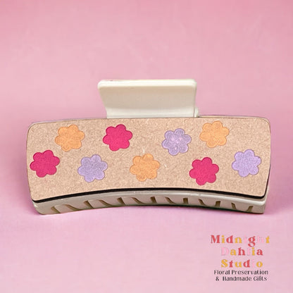 a claw hair clip with daisy shapes in pink orange and lavender purple