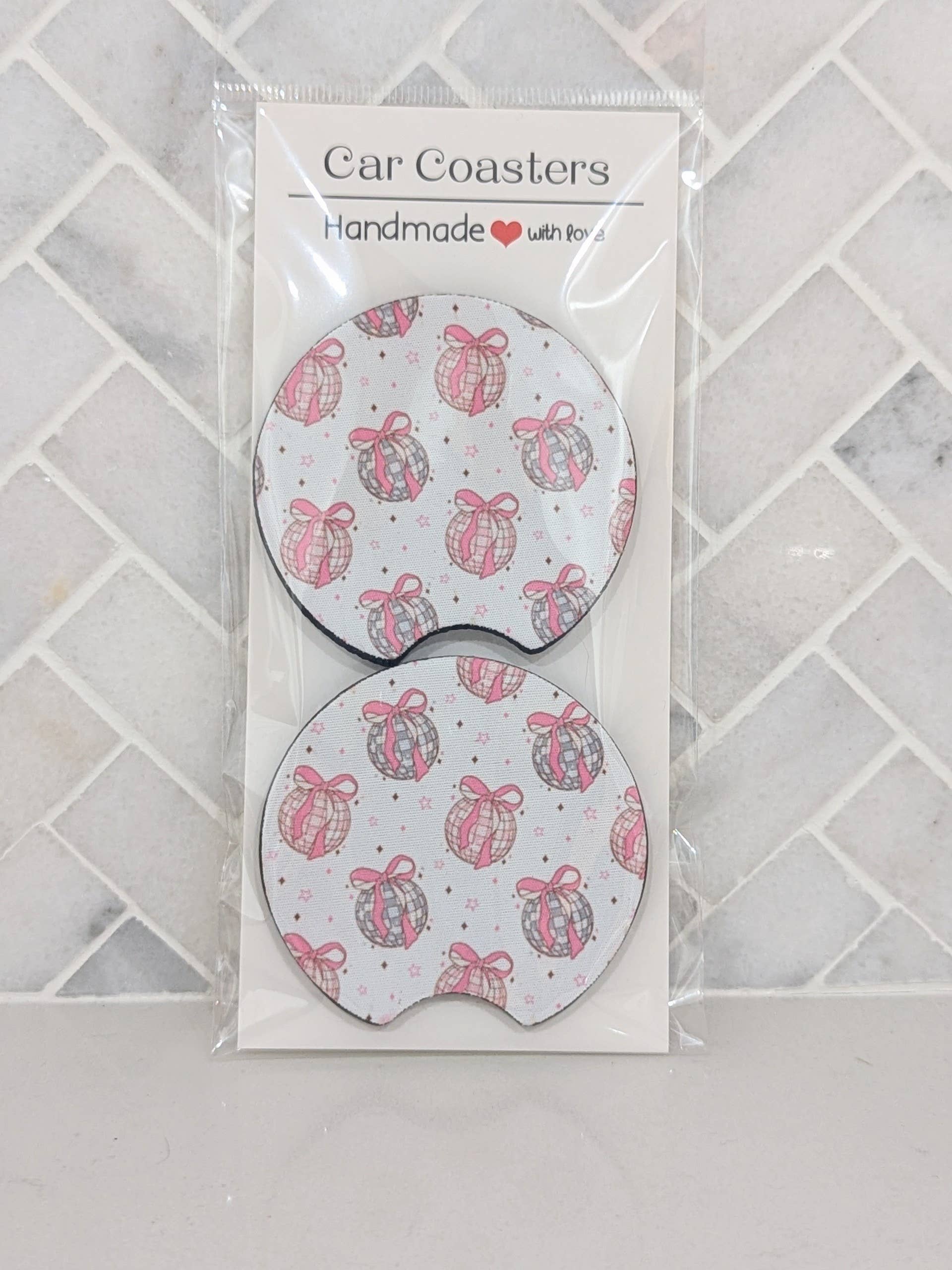 Car coasters with pink and gray designs in packaging on a tiled surface