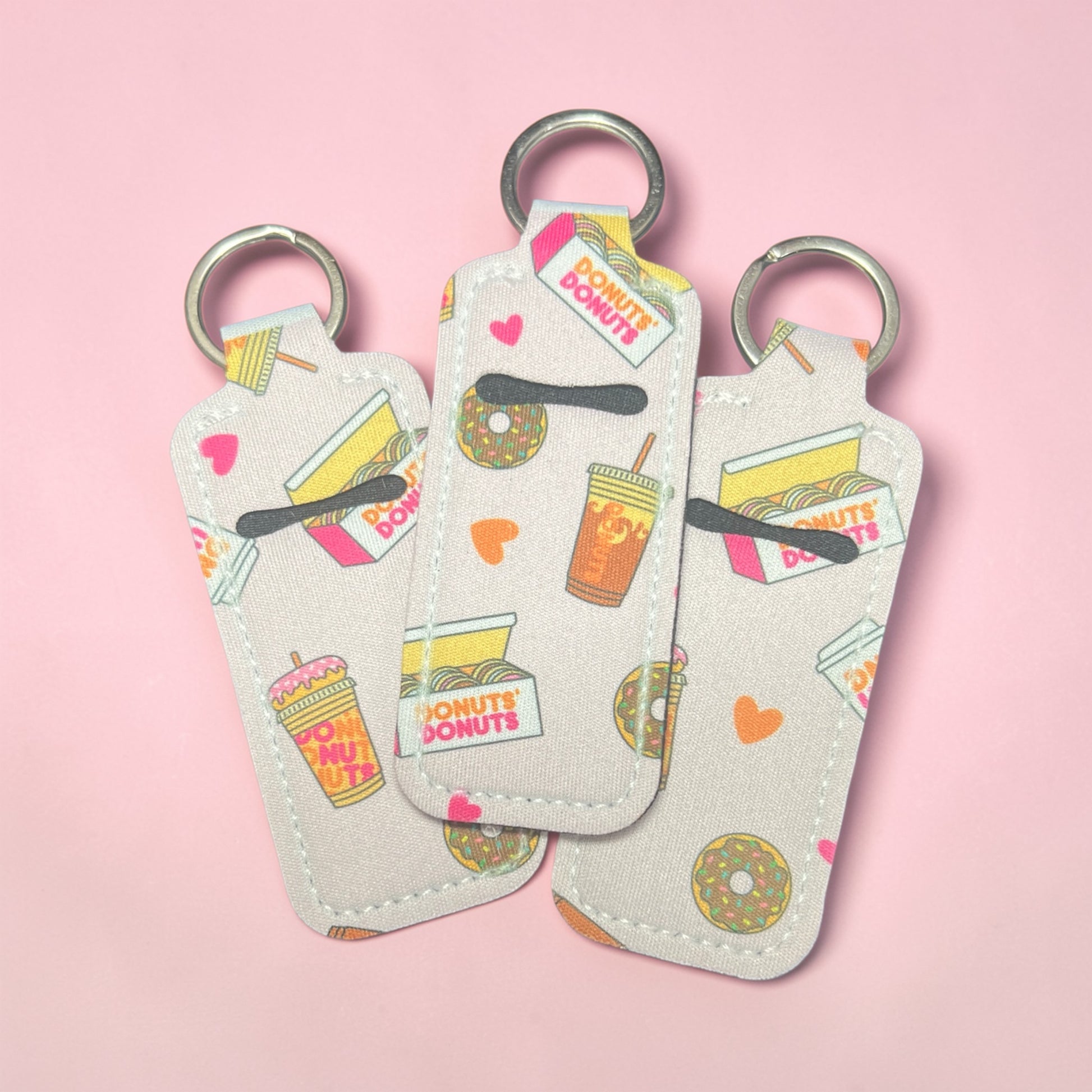 Three keychains with donut and coffee design on a pink background